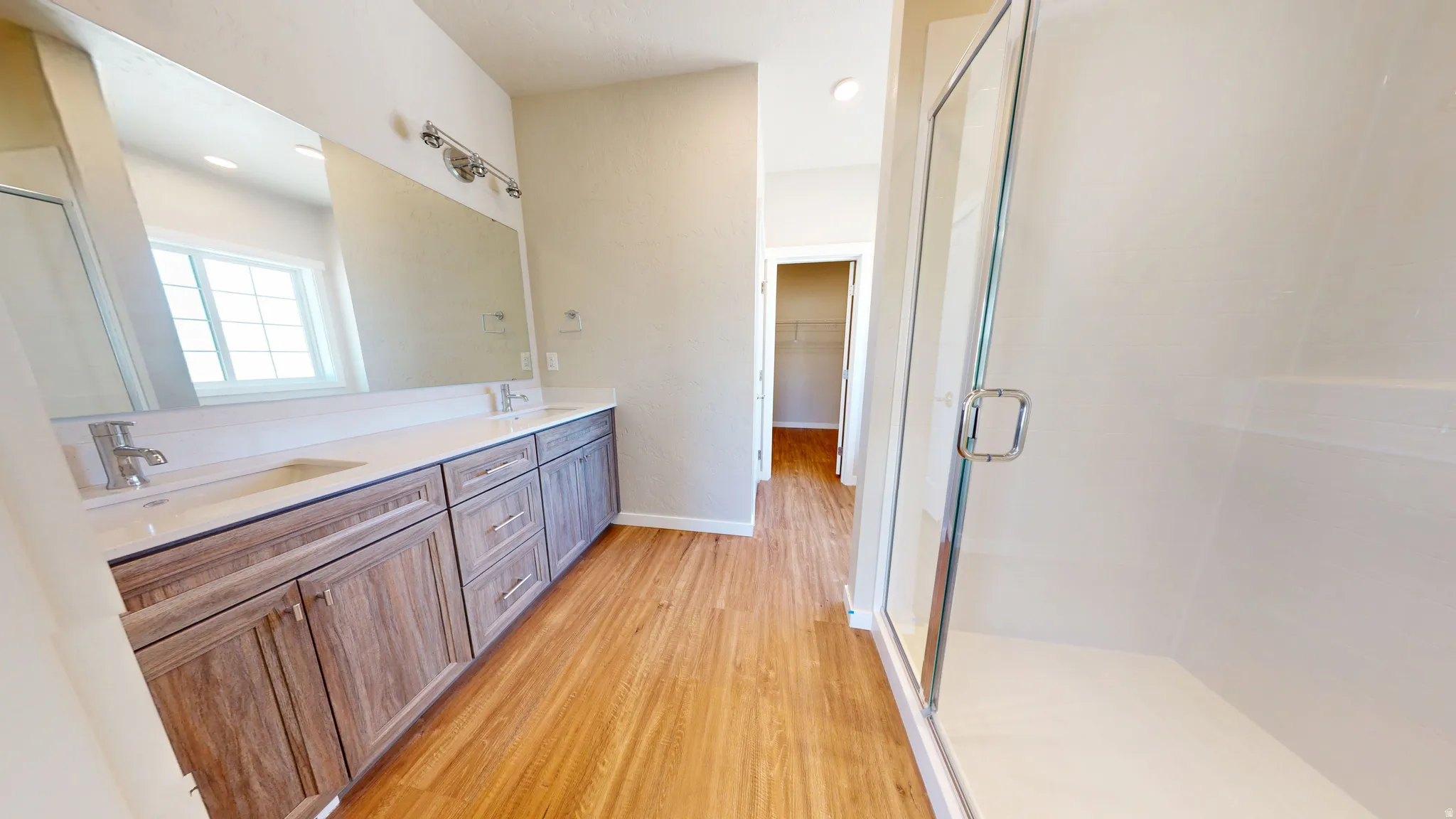 Bathroom with light wood finished floors, double vanity, a walk in closet, and a shower stall