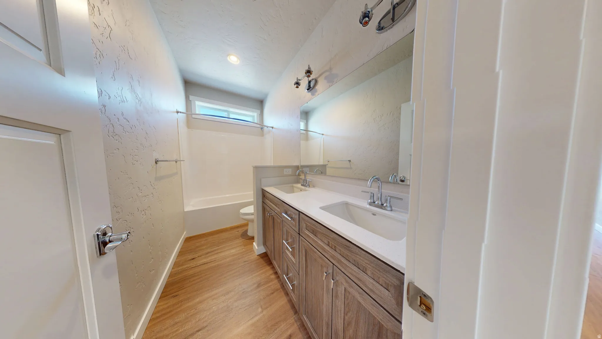 Full bath featuring double vanity, light wood finished floors, a textured wall, and tub / shower combination
