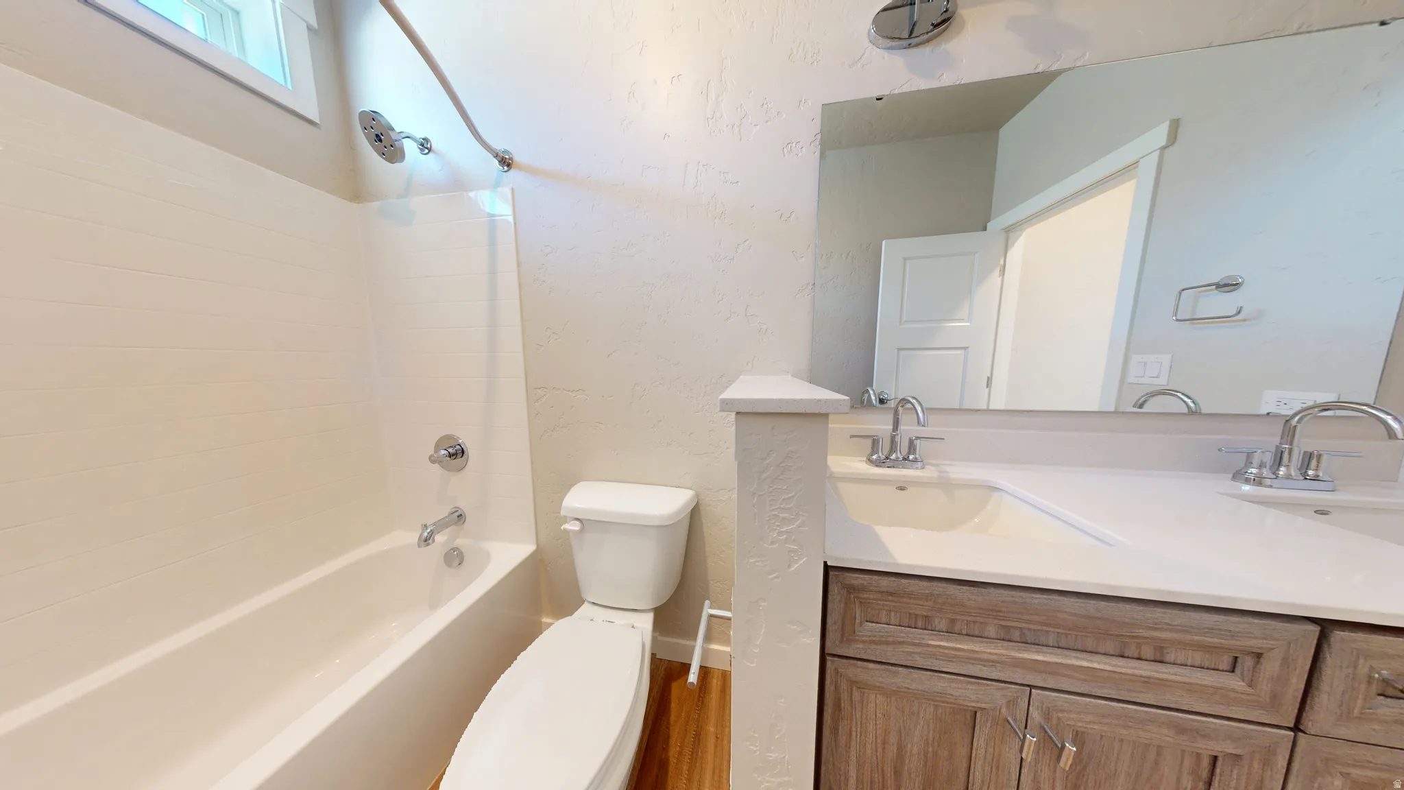 Full bathroom with a textured wall, double vanity, shower / washtub combination, and wood finished floors