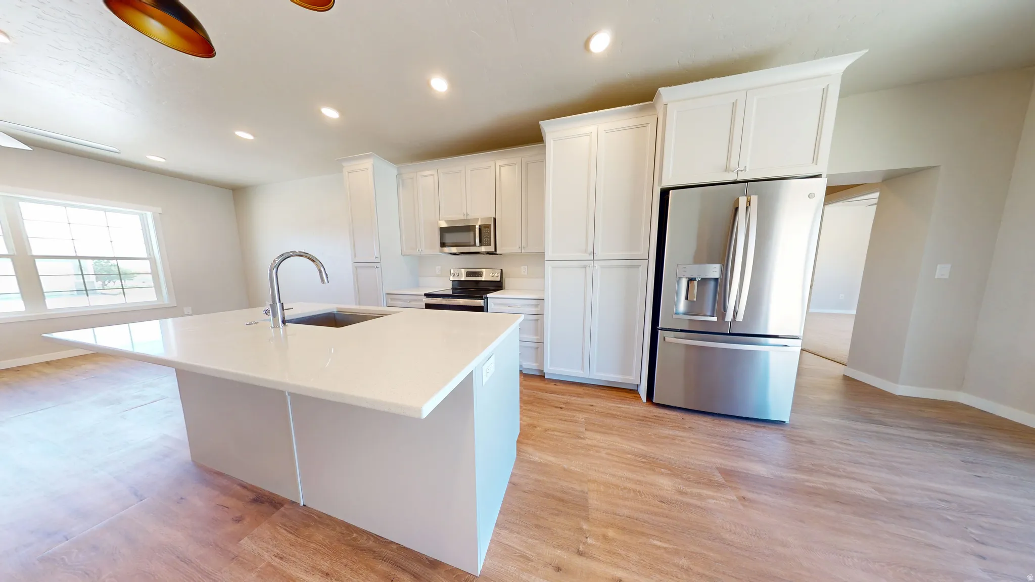 Kitchen featuring appliances with stainless steel finishes, white cabinetry, recessed lighting, a center island with sink, and light wood-style flooring