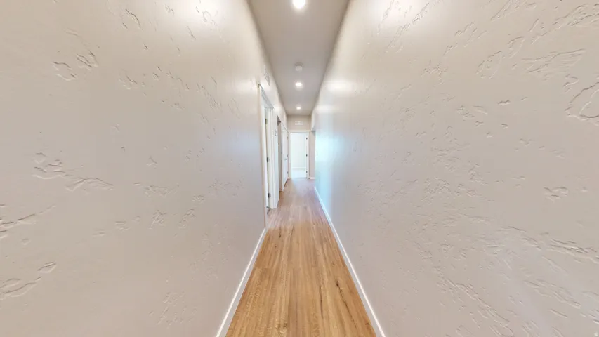 Corridor with a textured wall, recessed lighting, and light wood-type flooring