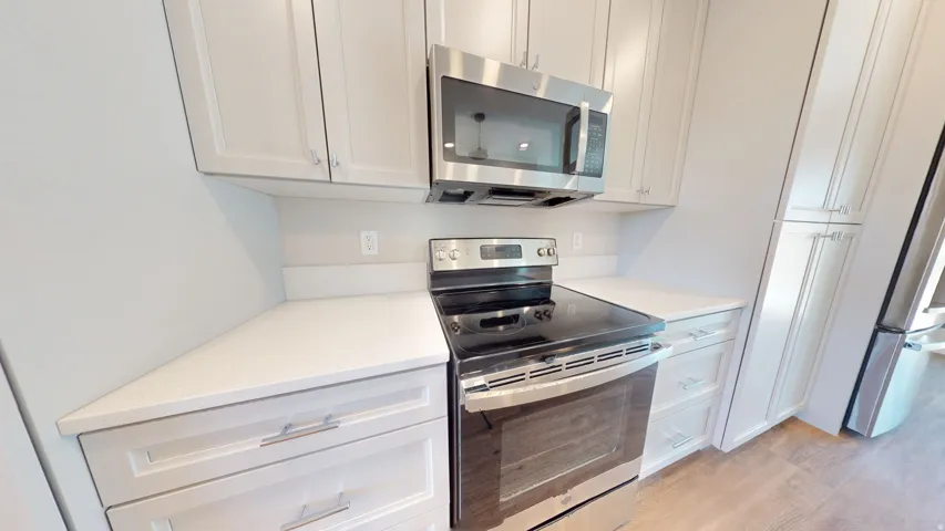 Kitchen with appliances with stainless steel finishes, light wood-style floors, white cabinetry, and light stone counters