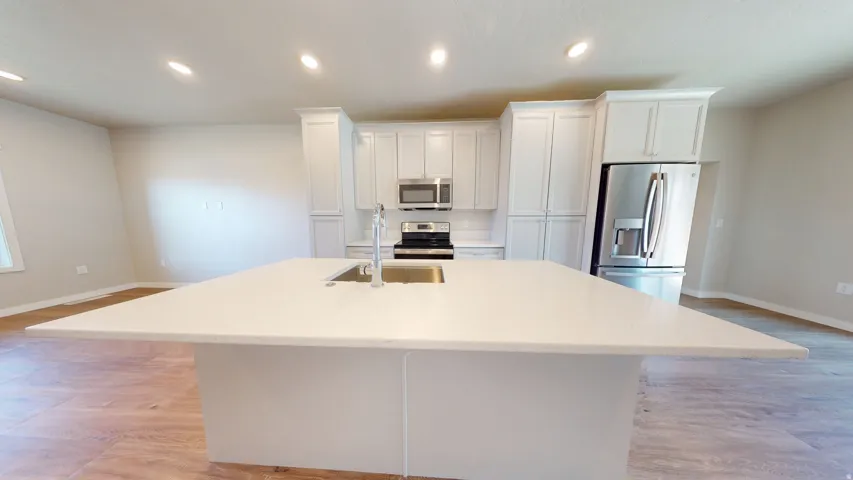 Kitchen with recessed lighting, stainless steel appliances, white cabinetry, light wood-type flooring, and a center island with sink