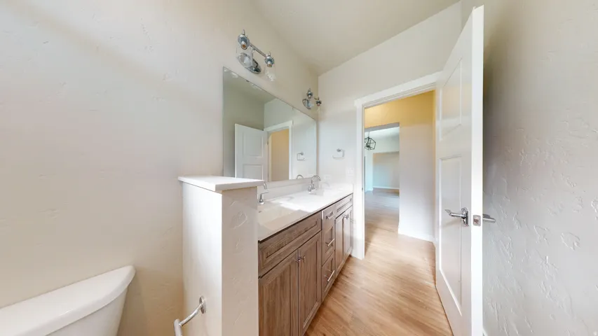 Bathroom featuring a textured wall, double vanity, and light wood-style floors