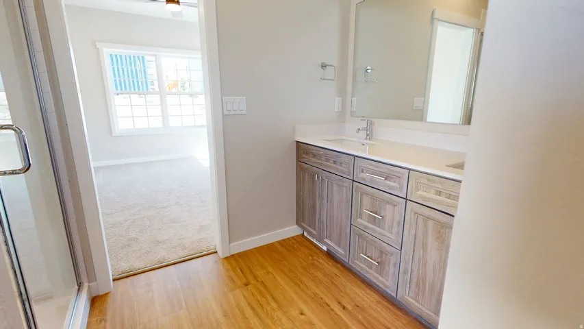 Bathroom featuring double vanity, light wood-type flooring, and a shower with door