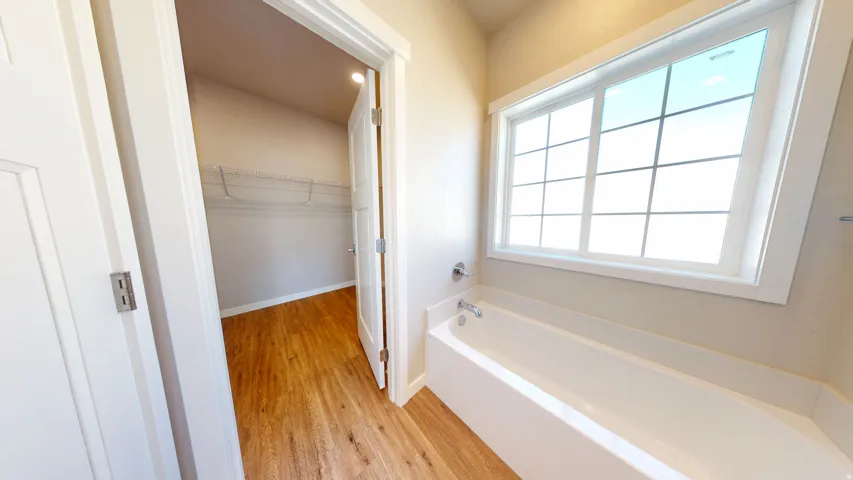 Full bathroom with a bath, a spacious closet, and light wood-style flooring