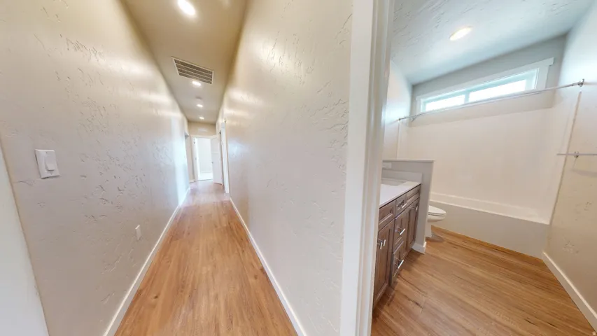 Hall featuring a textured wall, light wood finished floors, and recessed lighting