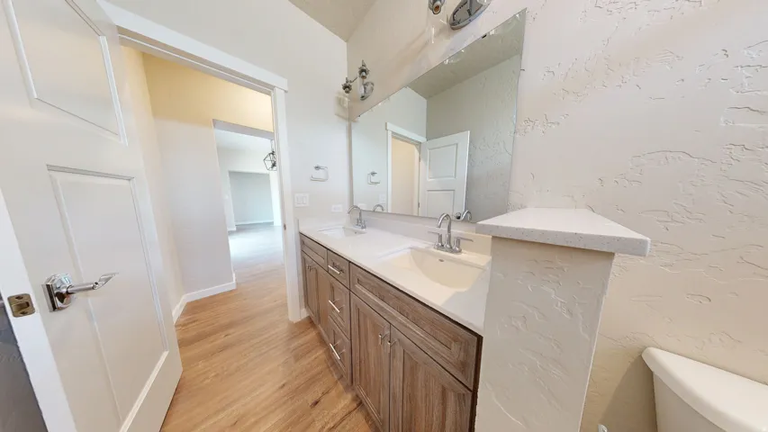 Bathroom with double vanity, light wood-type flooring, and a textured wall