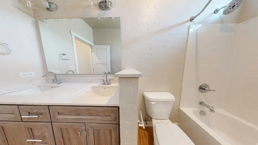 Bathroom featuring a textured wall, double vanity, and bathing tub / shower combination