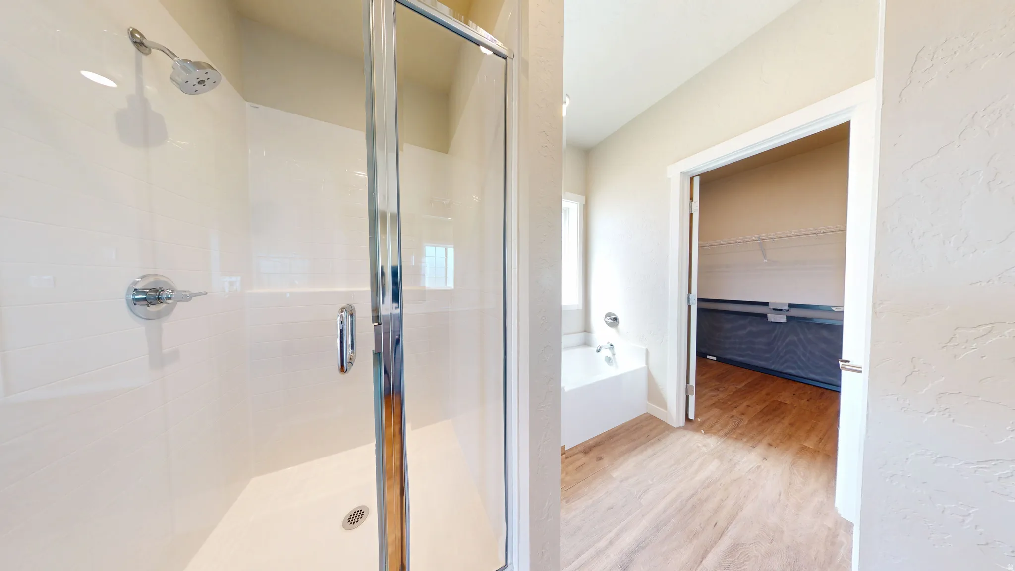 Full bath featuring light wood-style floors, a stall shower, a garden tub, a walk in closet, and a textured wall