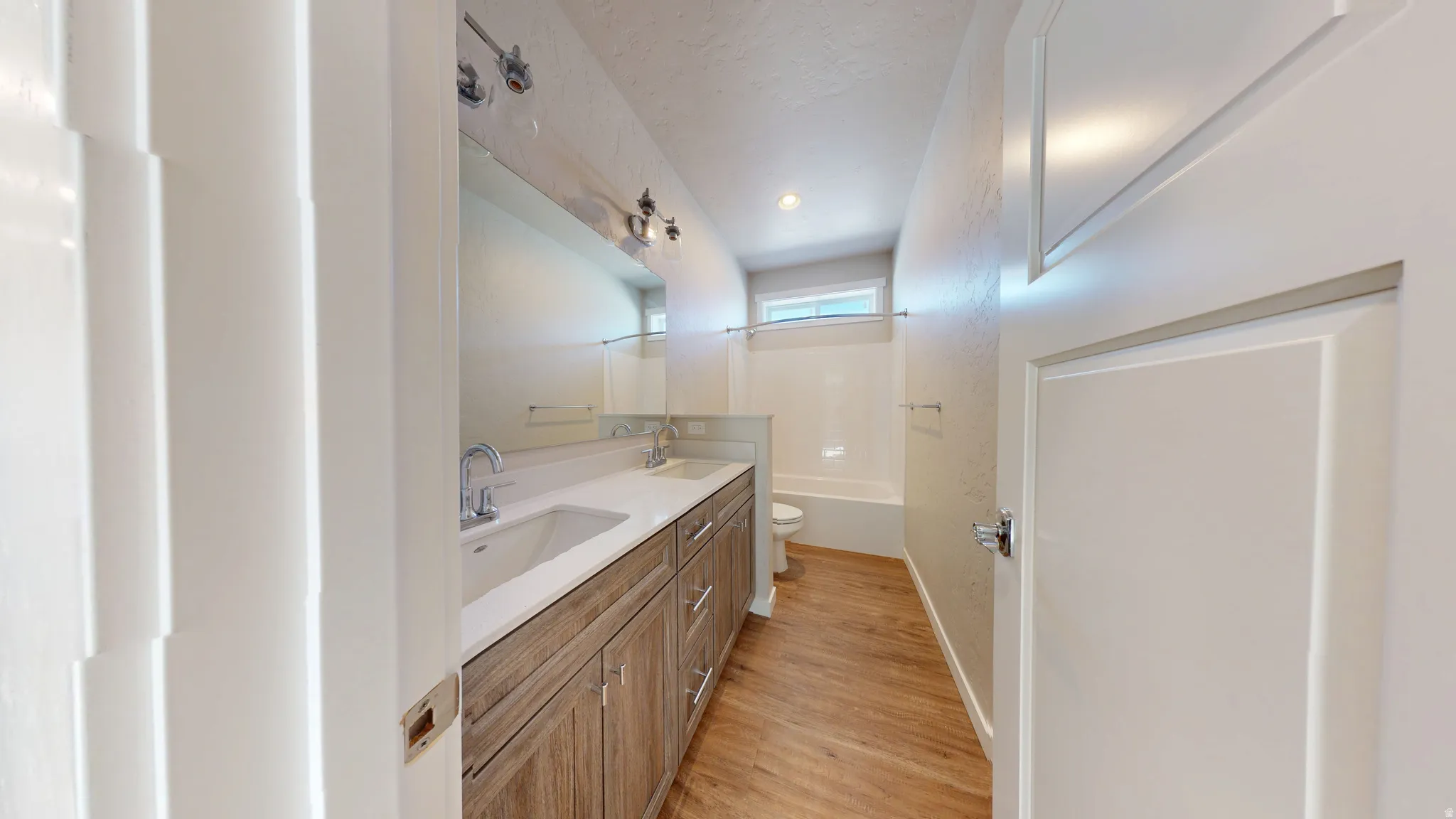 Bathroom with double vanity, light wood-type flooring, and shower / bath combination