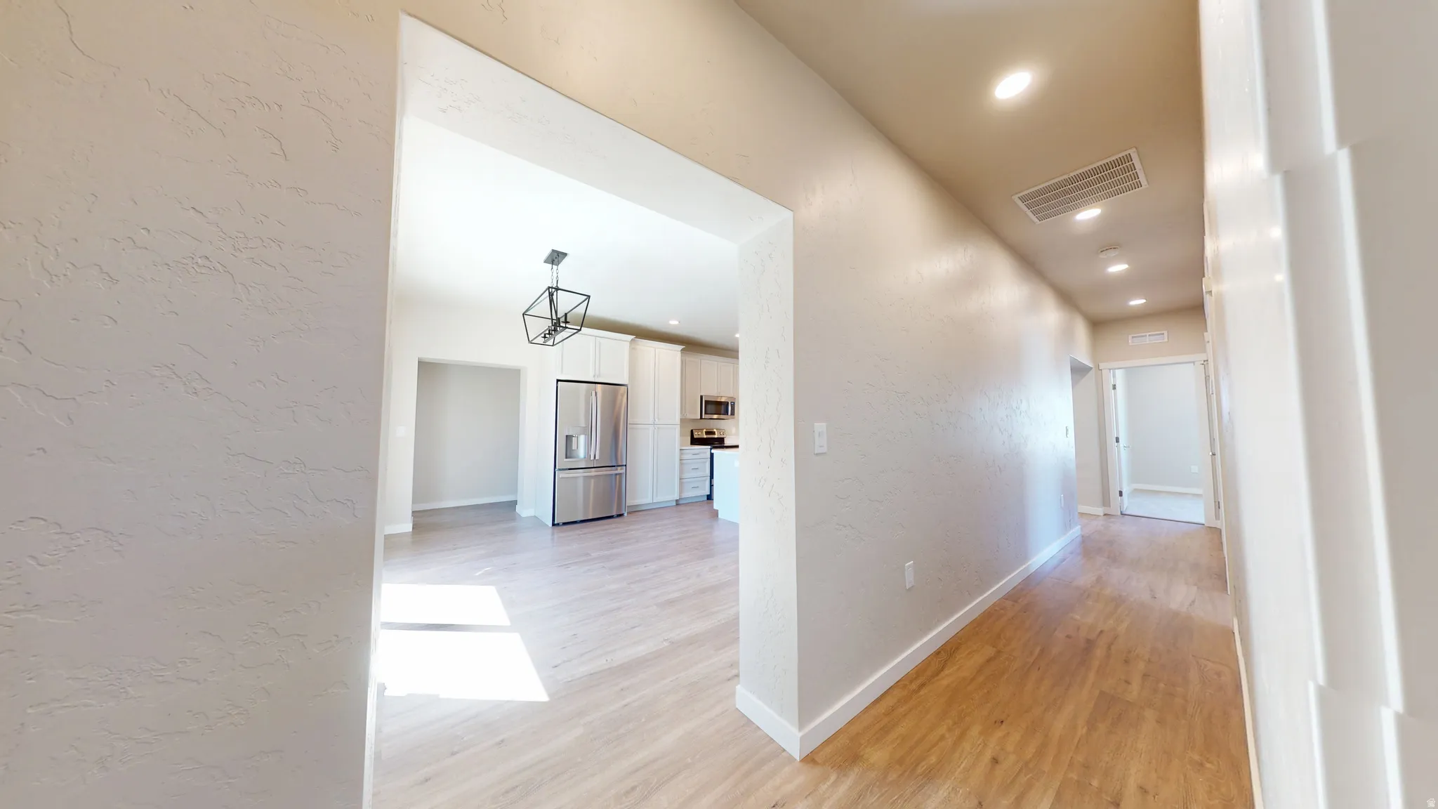 Hallway with a textured wall, light wood-type flooring, and recessed lighting
