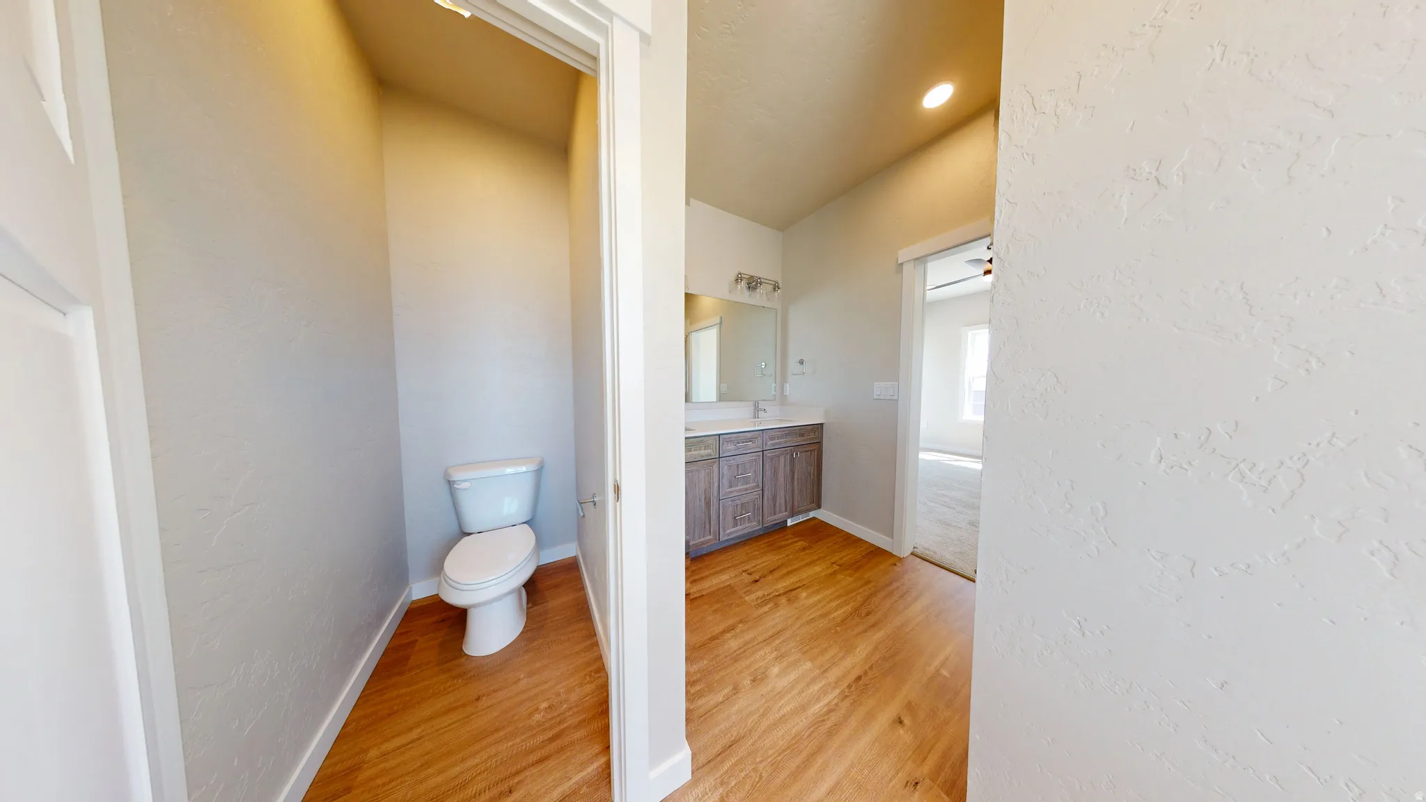 Bathroom with a textured wall, light wood finished floors, vanity, and recessed lighting