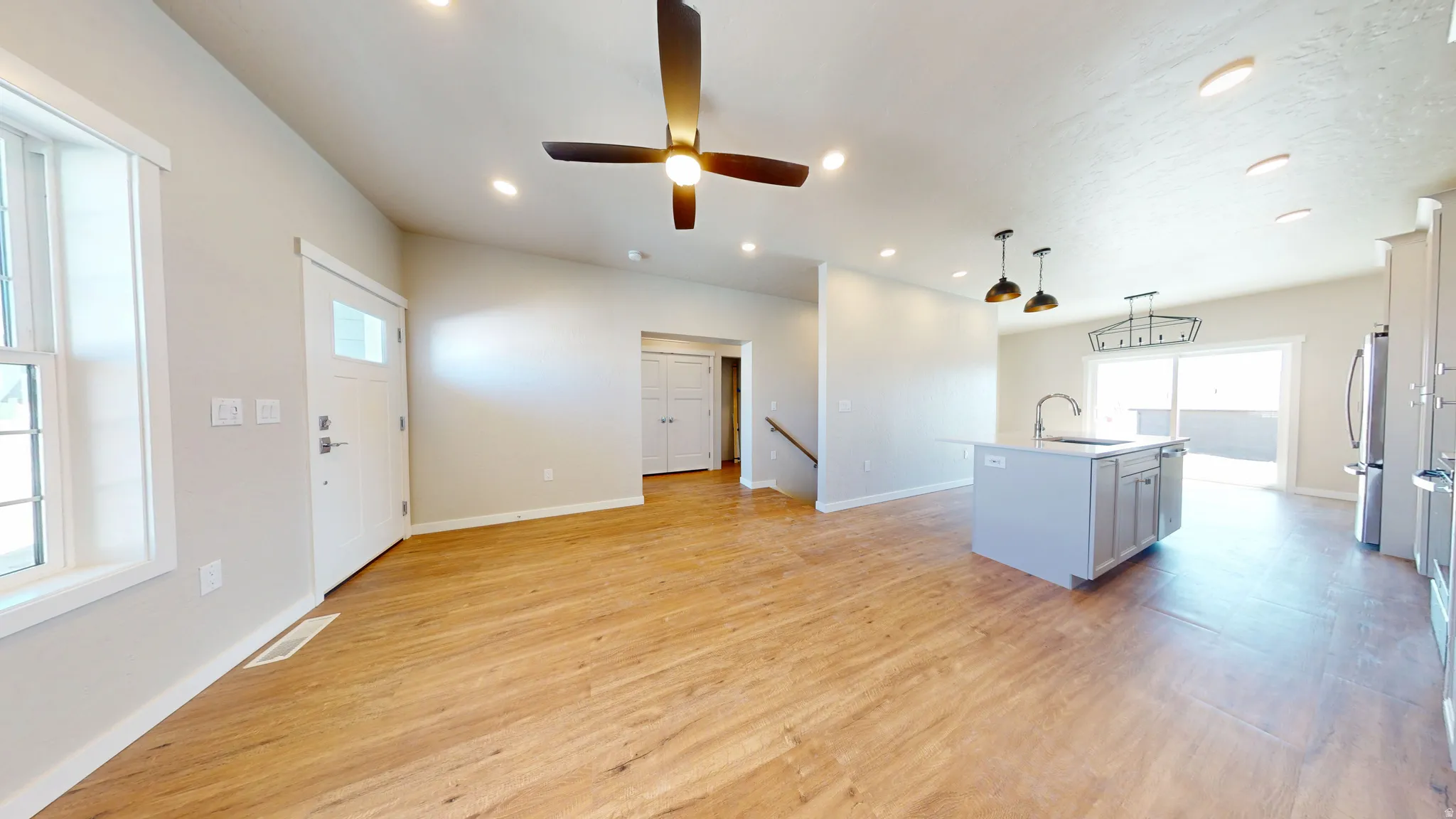 Kitchen featuring a center island with sink, pendant lighting, light wood-style floors, stainless steel appliances, and a ceiling fan