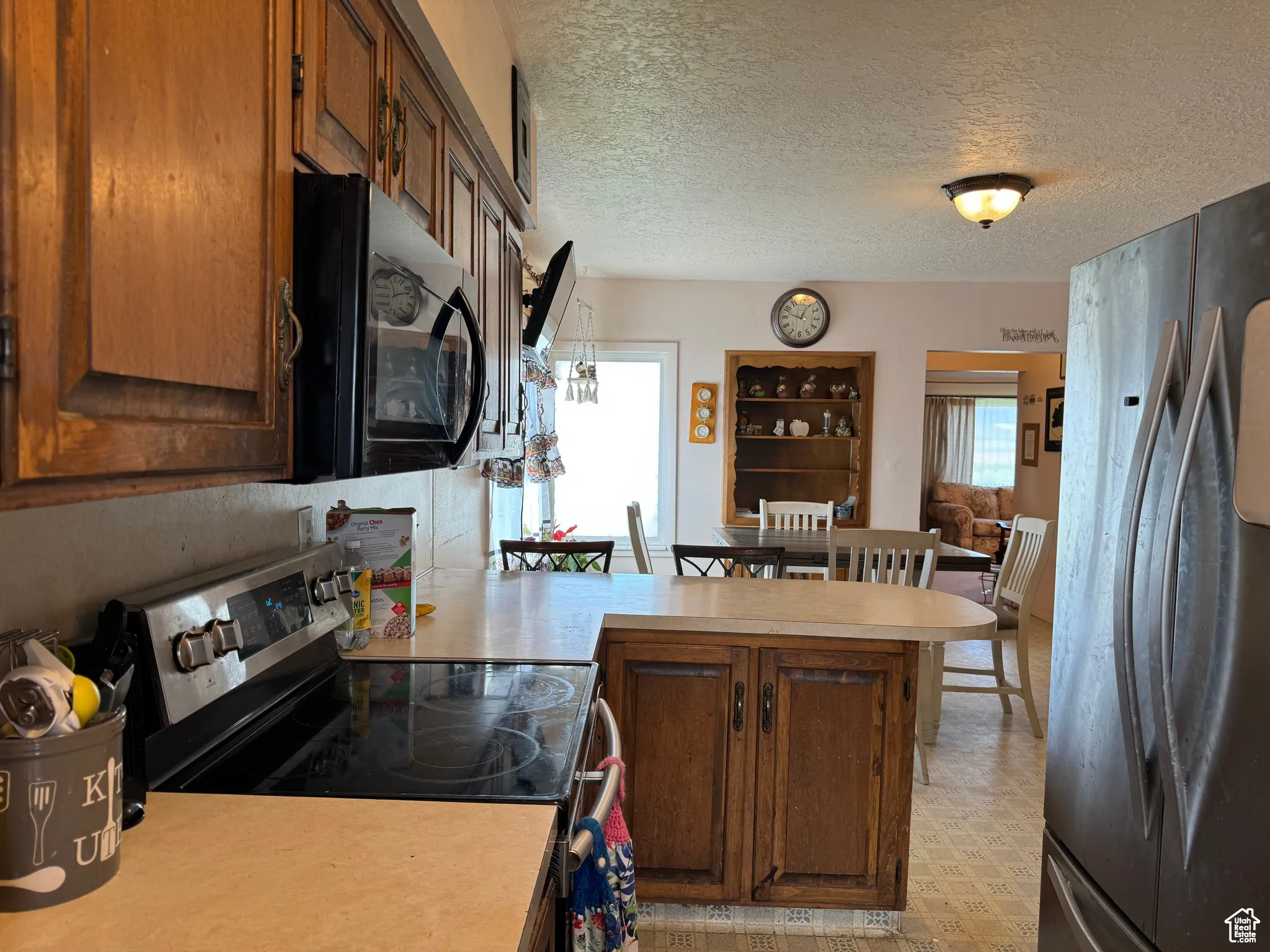 Kitchen featuring kitchen peninsula, a textured ceiling, electric range oven, and stainless steel refrigerator