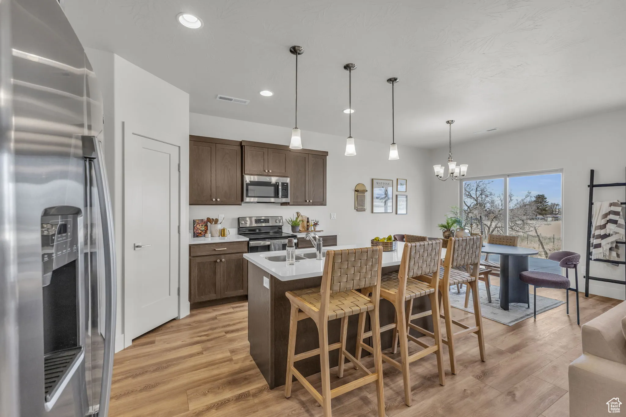 Kitchen featuring hanging light fixtures, stainless steel appliances, an inviting chandelier, an island with sink, and dark brown cabinets