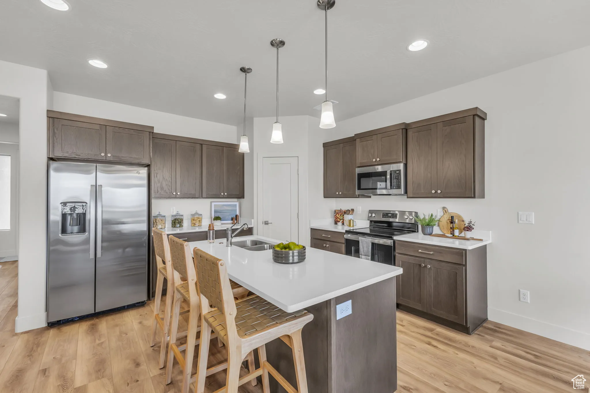 Kitchen with a kitchen bar, light wood-type flooring, stainless steel appliances, decorative light fixtures, and an island with sink