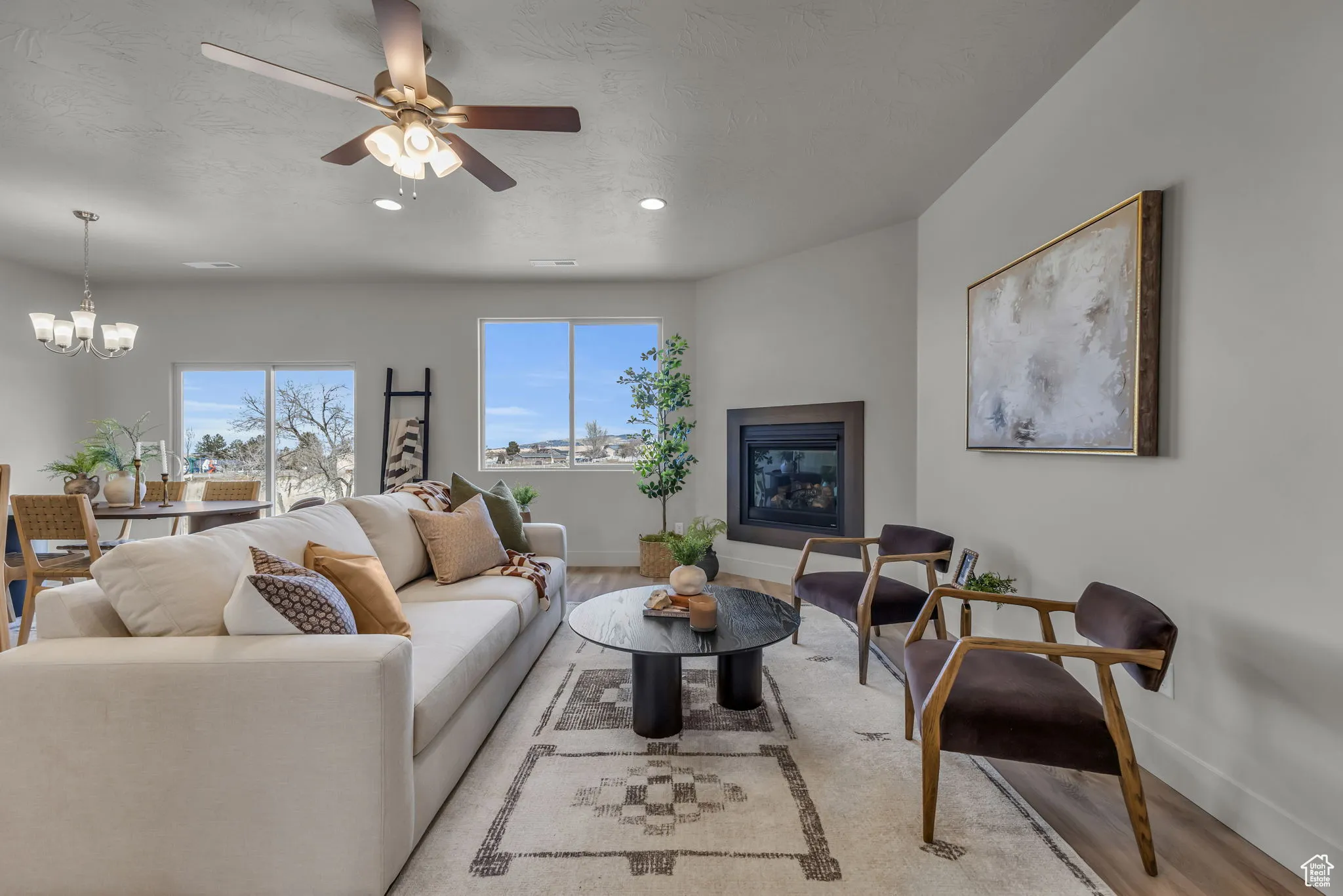 Living room with ceiling fan with notable chandelier and light hardwood / wood-style floors