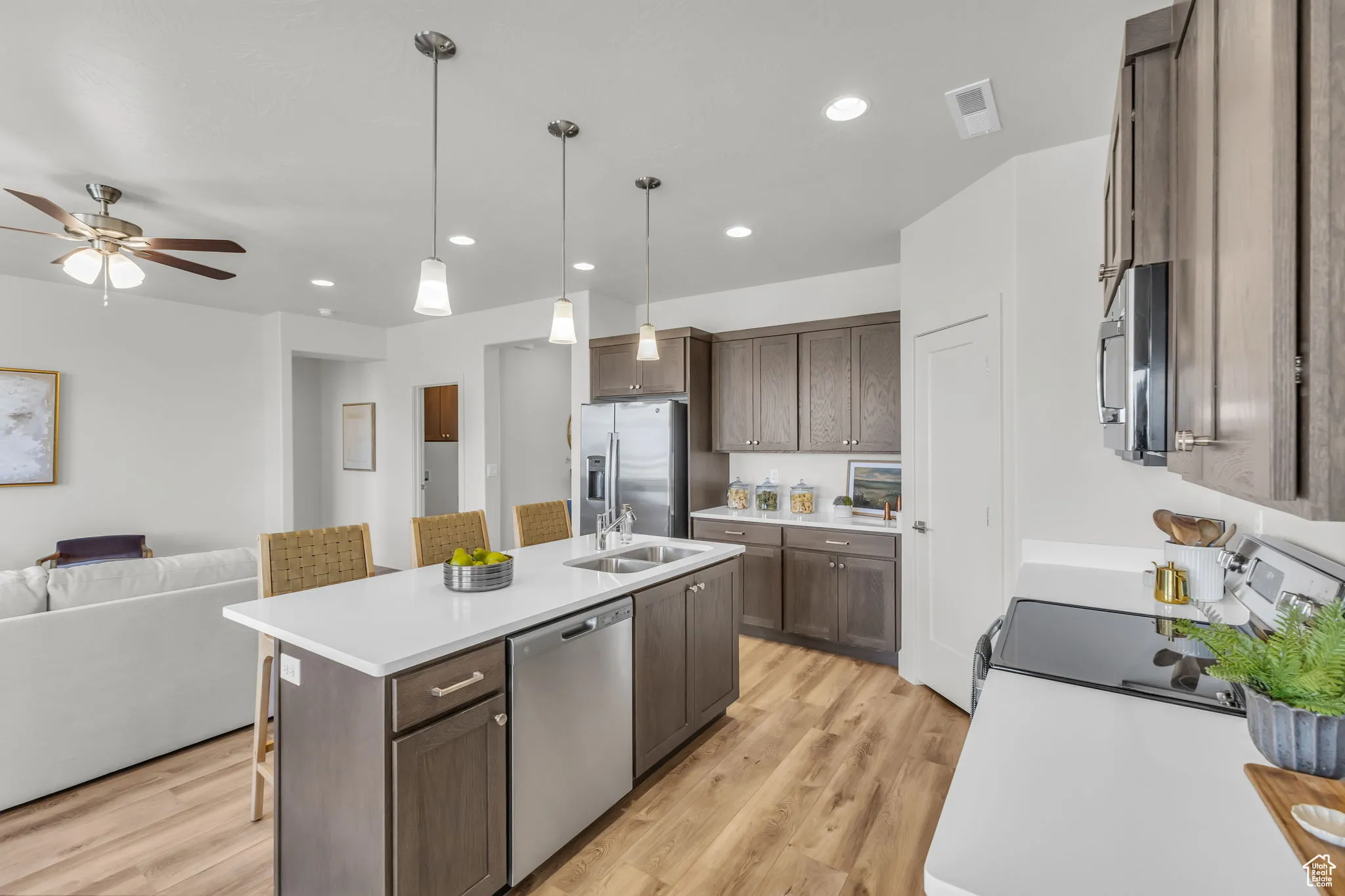Kitchen featuring light hardwood / wood-style flooring, ceiling fan, an island with sink, appliances with stainless steel finishes, and decorative light fixtures