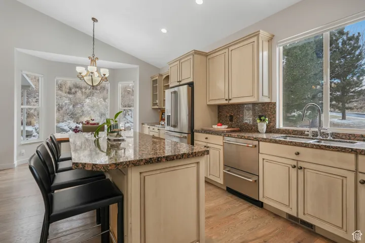 Kitchen with sink, a chandelier, high quality fridge, decorative backsplash, and a breakfast bar