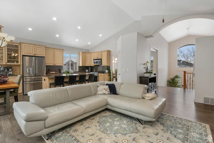 Living room with a chandelier, dark wood-type flooring, and vaulted ceiling