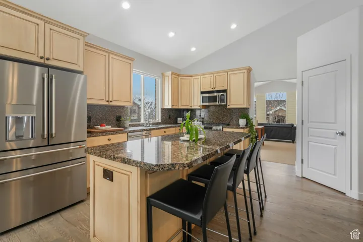 Kitchen featuring appliances with stainless steel finishes, dark stone counters, vaulted ceiling, a kitchen island, and light wood-type flooring