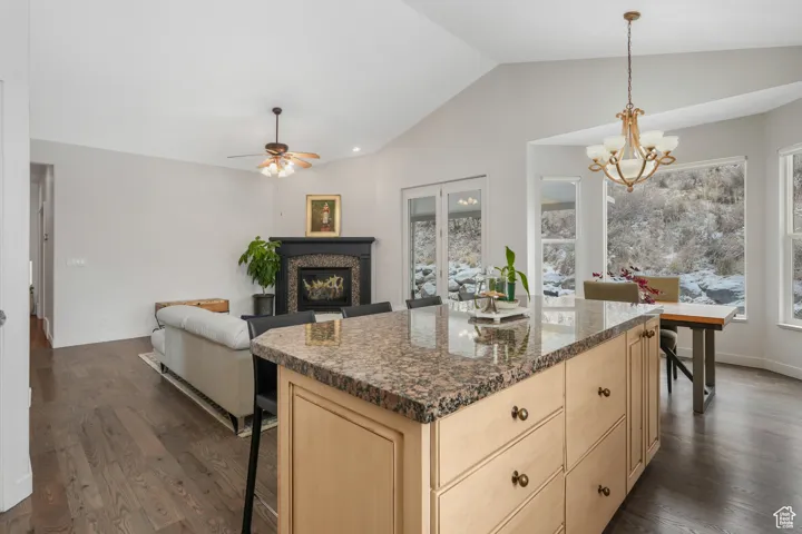 Kitchen with a kitchen breakfast bar, ceiling fan with notable chandelier, lofted ceiling, and dark stone countertops