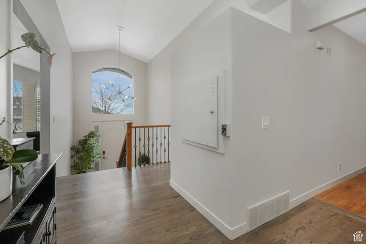 Hallway featuring dark hardwood / wood-style floors, lofted ceiling, and an inviting chandelier