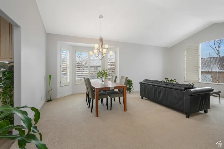 Carpeted dining space featuring lofted ceiling and a notable chandelier