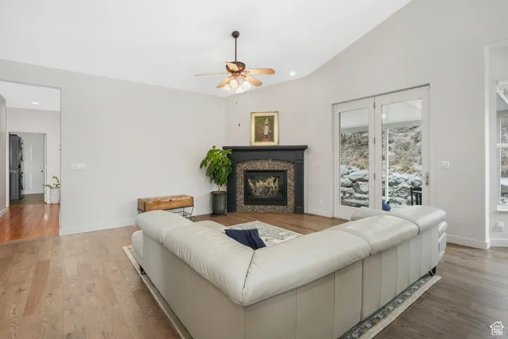 Living room with ceiling fan, wood-type flooring, a tile fireplace, and vaulted ceiling