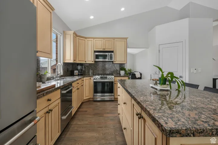 Kitchen with decorative backsplash, a kitchen island, stainless steel appliances, and vaulted ceiling