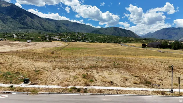 Expansive undeveloped land featuring a mountain backdrop, partial fencing, and distant residential structures