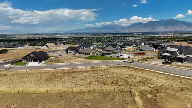 Expansive property featuring developing residential community, paved roadways, and distant mountain ranges under a partly cloudy sky