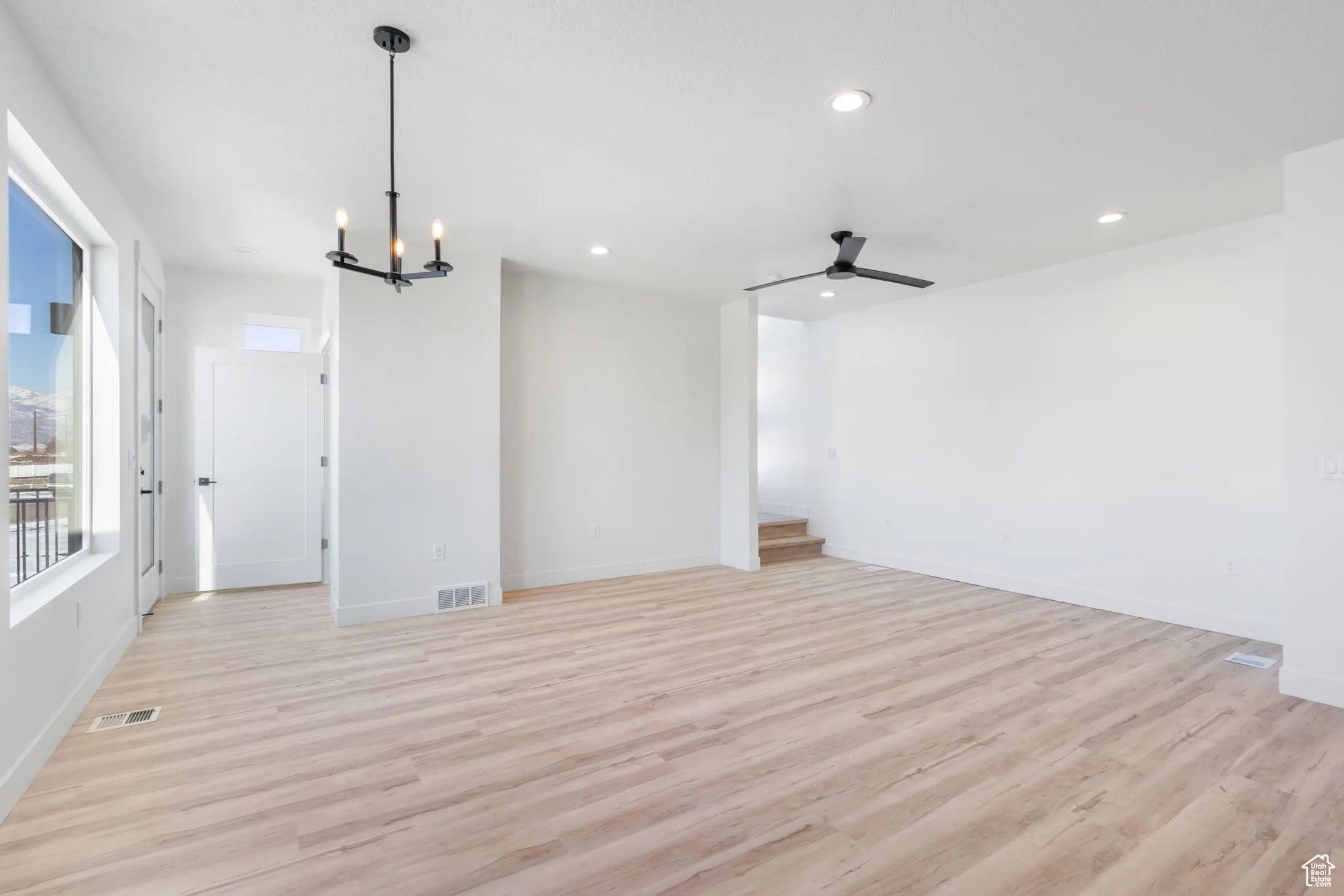 Spare room featuring ceiling fan with notable chandelier and light hardwood / wood-style floors