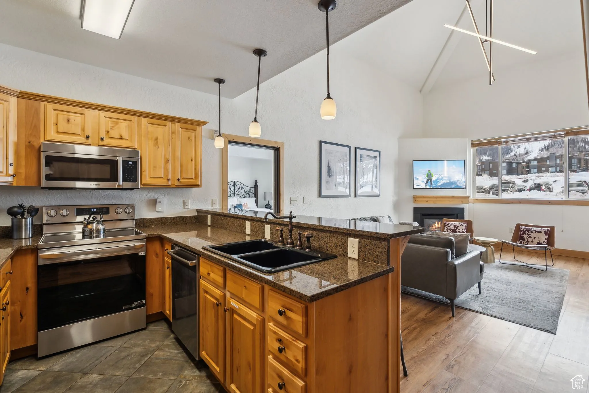 Kitchen with dark stone countertops, appliances with stainless steel finishes, hanging light fixtures, kitchen peninsula, and sink