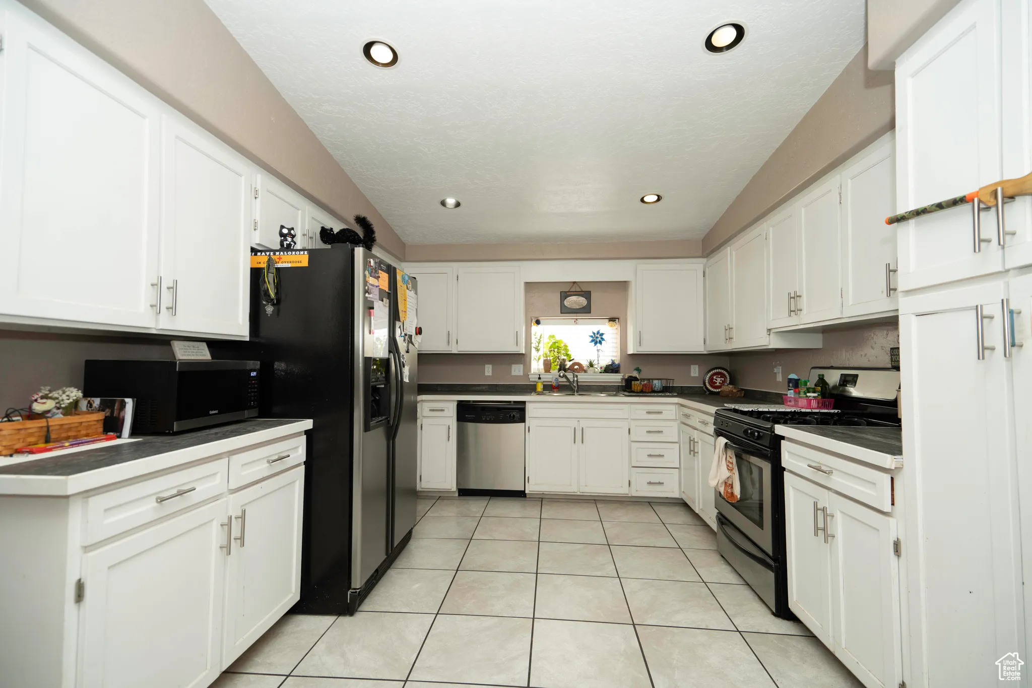 Kitchen featuring appliances with stainless steel finishes, sink, light tile patterned floors, and white cabinets