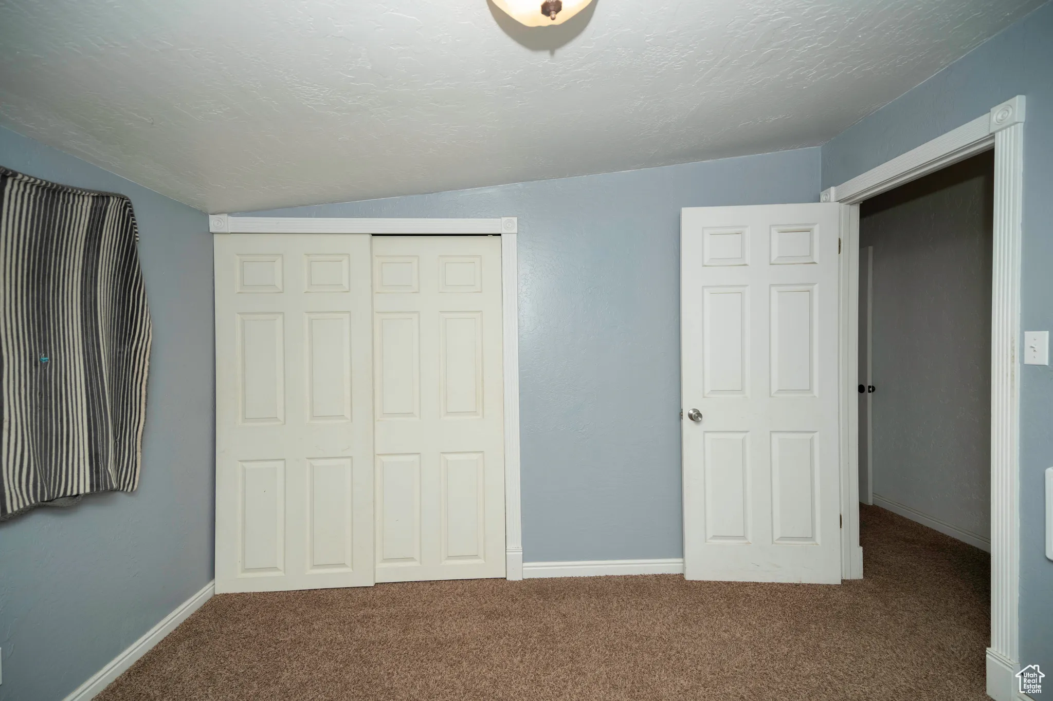 Unfurnished bedroom with carpet floors, vaulted ceiling, a closet, and a textured ceiling
