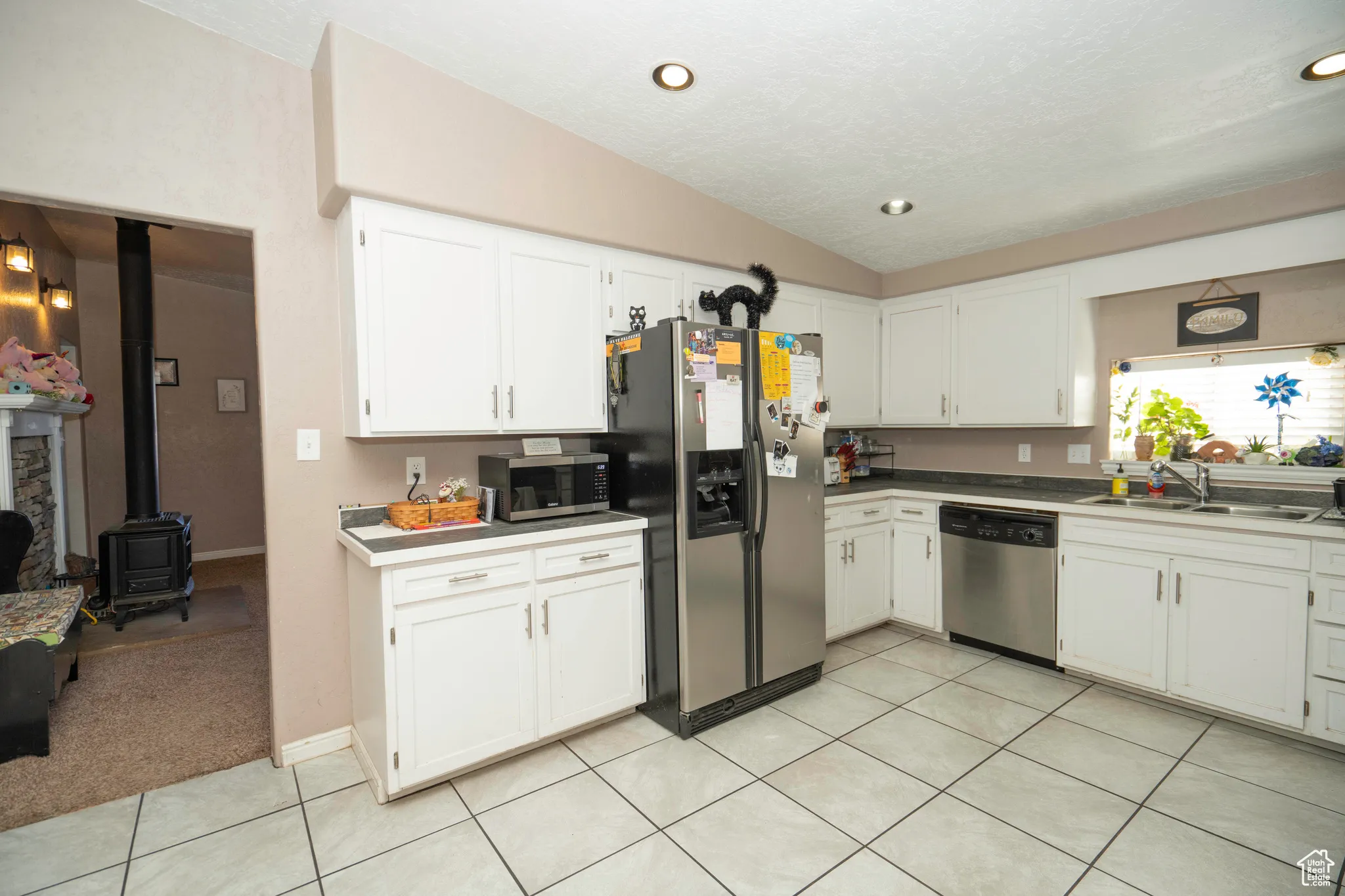 Kitchen with lofted ceiling, sink, white cabinetry, a wood stove, and stainless steel appliances