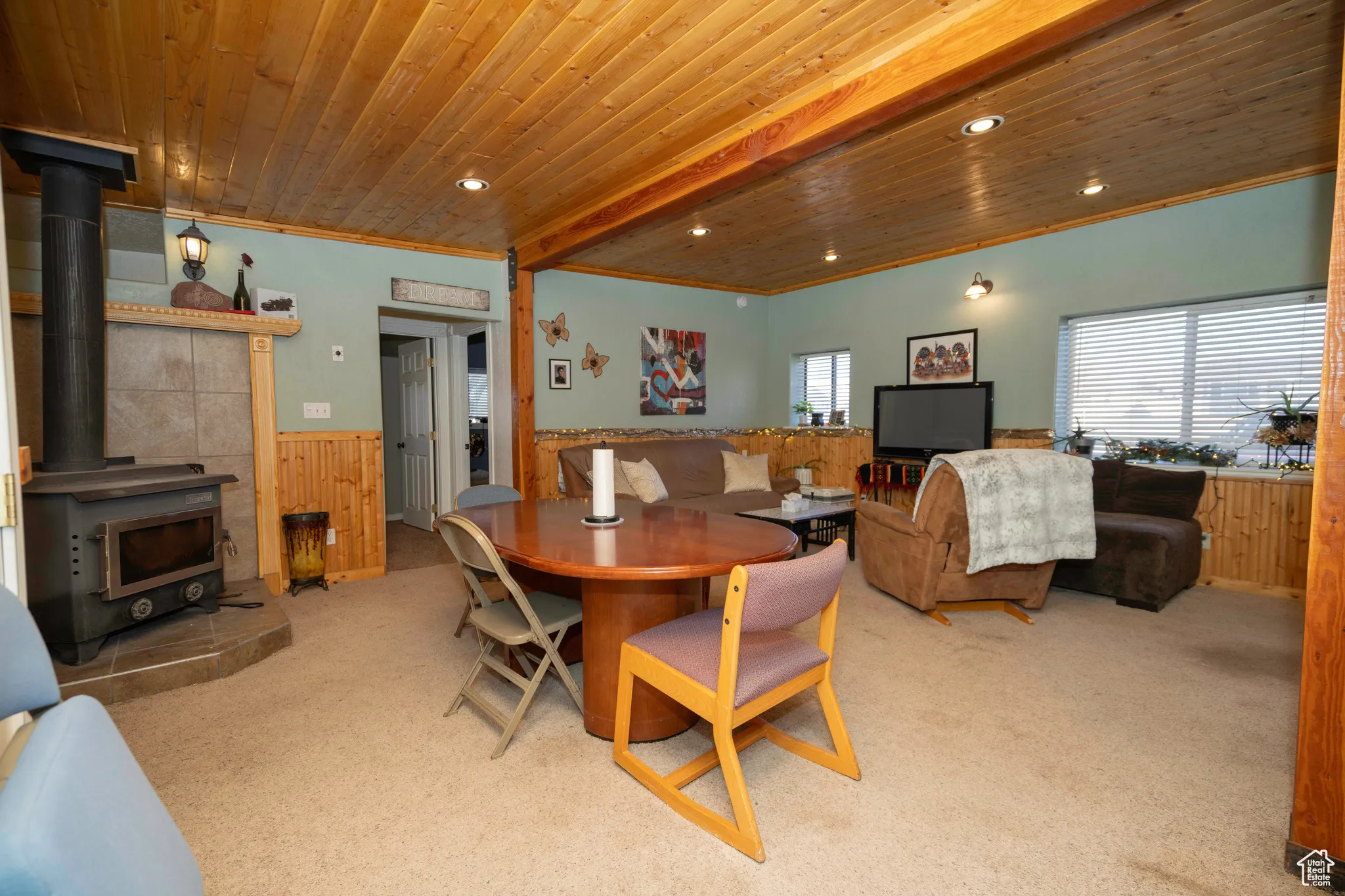 Carpeted dining space featuring crown molding, a wood stove, wooden ceiling, and wooden walls
