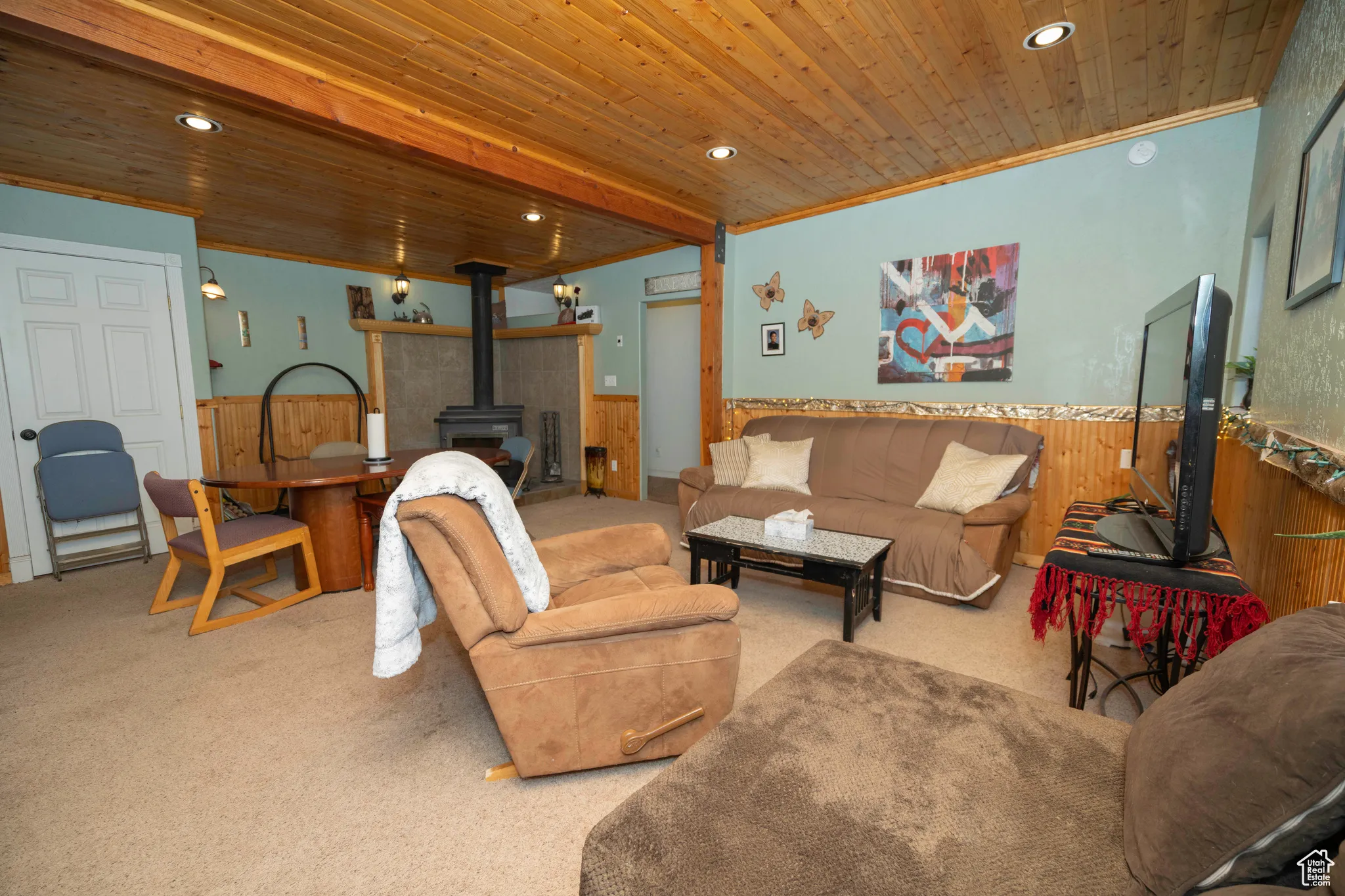 Carpeted living room featuring ornamental molding, a wood stove, wooden ceiling, and wooden walls