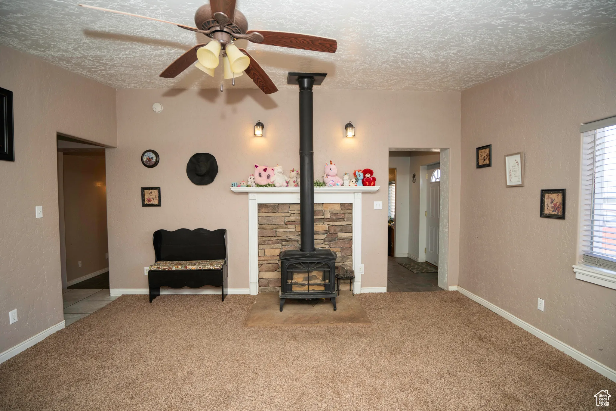 Living room with light carpet, ceiling fan, a textured ceiling, and a wood stove