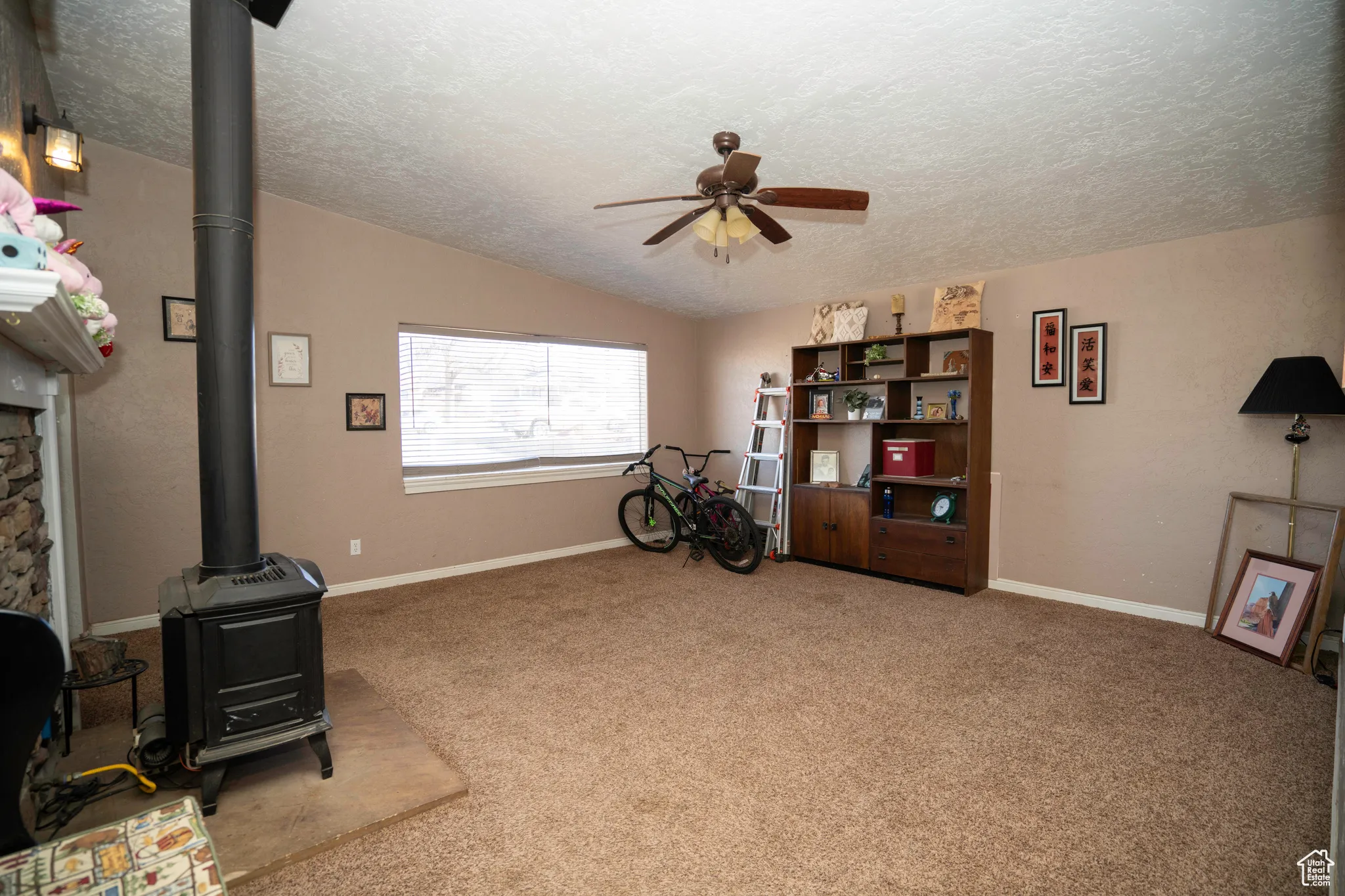 Misc room featuring vaulted ceiling, a wood stove, carpet, ceiling fan, and a textured ceiling