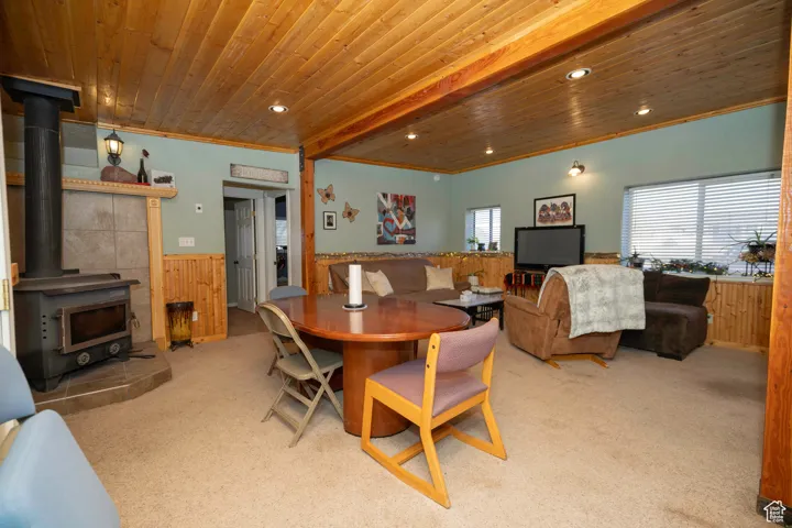 Carpeted dining space featuring crown molding, a wood stove, wooden ceiling, and wooden walls