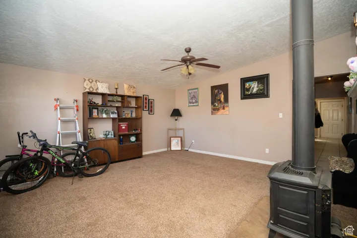 Miscellaneous room with ceiling fan, light carpet, a textured ceiling, and a wood stove