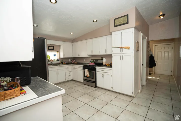 Kitchen featuring white cabinetry, stainless steel range with gas cooktop, sink, and vaulted ceiling
