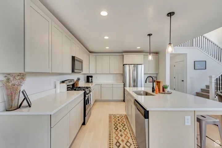 Kitchen featuring light hardwood / wood-style flooring, an island with sink, sink, decorative light fixtures, and appliances with stainless steel finishes