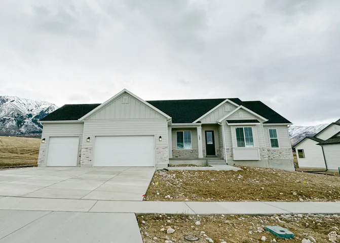 View of front of home with board and batten siding, a garage, stone siding, and driveway