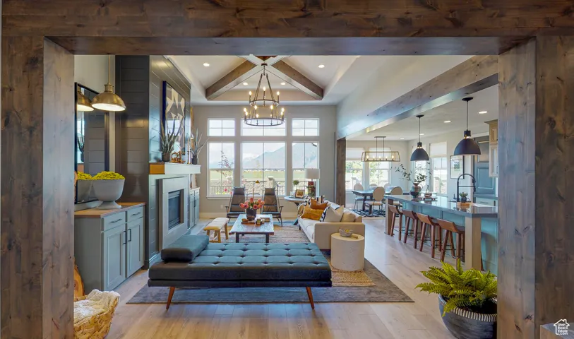Living room with a notable chandelier, a wealth of natural light, beamed ceiling, and light wood-type flooring