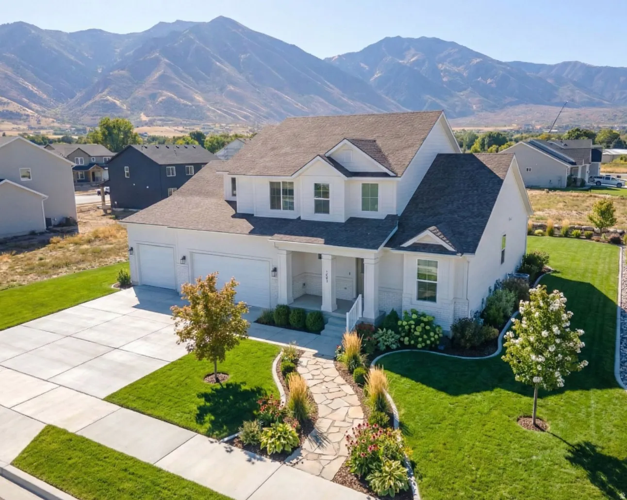 Contemporary two-story residence featuring a white exterior with dark roof, an attached three-car garage, and a stone walkway
