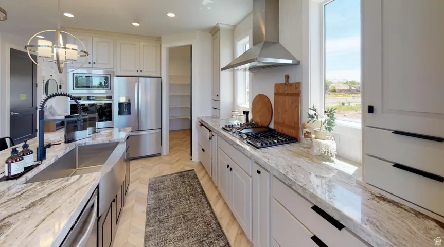 Kitchen featuring pendant lighting, light stone countertops, wall chimney exhaust hood, and appliances with stainless steel finishes